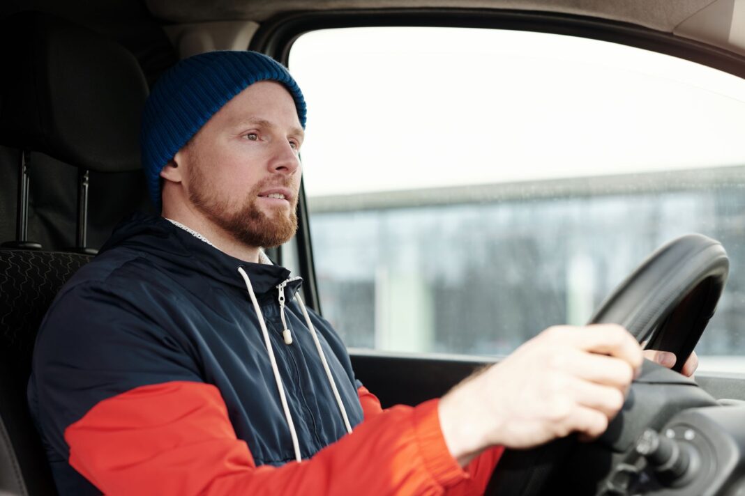Brodaty mężczyzna w czapce prowadzi auto zimą, skupiony na drodze