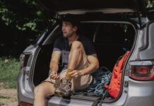 Jak przygotować auto do długiej trasy: kompleksowy poradnik przeglądu, wyposażenia i bezpieczeństwa Mężczyzna w bagażniku SUV-a wiąże buty przed długą podróżą