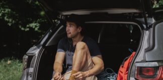 Mężczyzna w bagażniku SUV-a wiąże buty przed długą podróżą