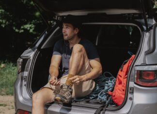 Mężczyzna w bagażniku SUV-a wiąże buty przed długą podróżą