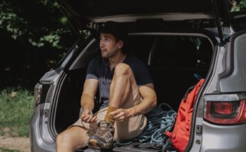 Jak przygotować auto do długiej trasy: kompleksowy poradnik przeglądu, wyposażenia i bezpieczeństwa Mężczyzna w bagażniku SUV-a wiąże buty przed długą podróżą
