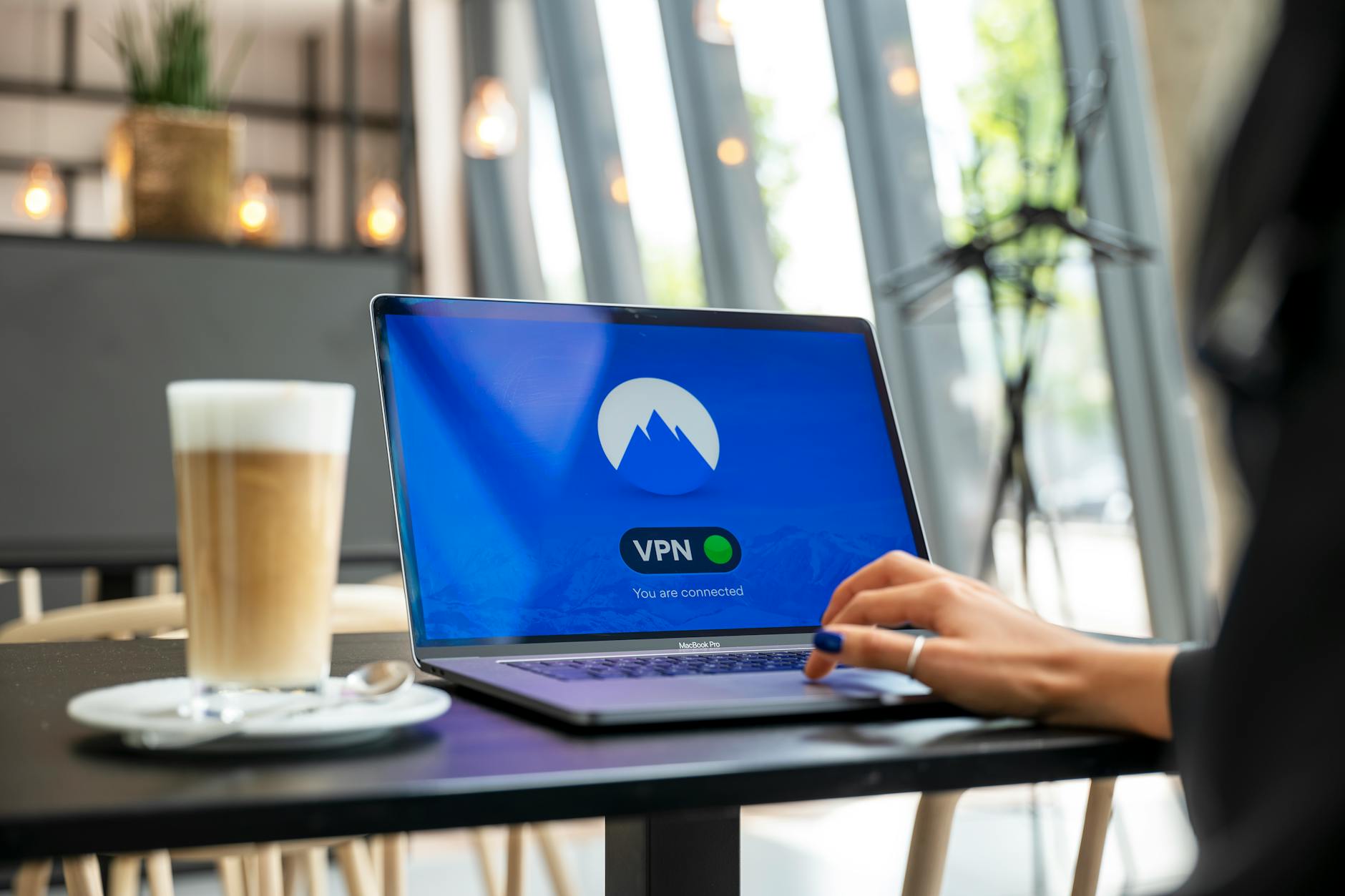 Osoba w kawiarni korzysta z laptopa z włączonym VPN dla bezpieczeństwa Wi‑Fi
