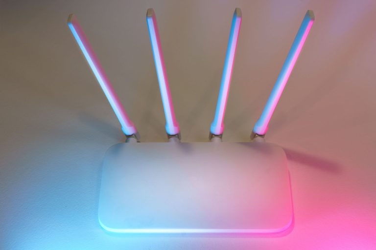 Biały router Wi‑Fi z czterema antenami w niebiesko-różowym świetle